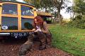 Vrouw in tweed jasje met hond naast een houten oldtimer op het gras