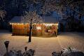 Houten tuinhuis met lichtjes in een besneeuwde tuin bij avond