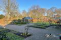 Lege moestuinbedden met buxusranden, bestrating en kas onder blauwe lucht