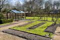 Aangeharkte moestuinbedden met graspaden en een tuinkas