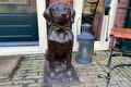Bronzen hondenbeeld met strik naast lantaarn bij de voordeur