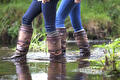 Twee vrouwen in jeans en hoge leren laarzen wadend door ondiep water