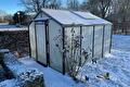 Aluminium tuinkas en heg bedekt met sneeuw in de tuin