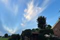Blauwe lucht met witte veerwolken boven boerderij en bomen