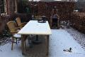 Besneeuwd terras met tafel, stoelen en gemetselde buitenoven