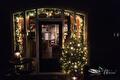 Verlichte voordeur met kerstboom en lichtslinger in het donker
