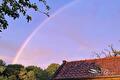 Regenboog boven een rood pannendak en bomen