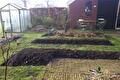 Omgespitte moestuinbedden met tuinkas en terras op de achtergrond