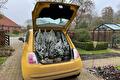 Gele auto met open kofferbak vol witte kerstplantjes